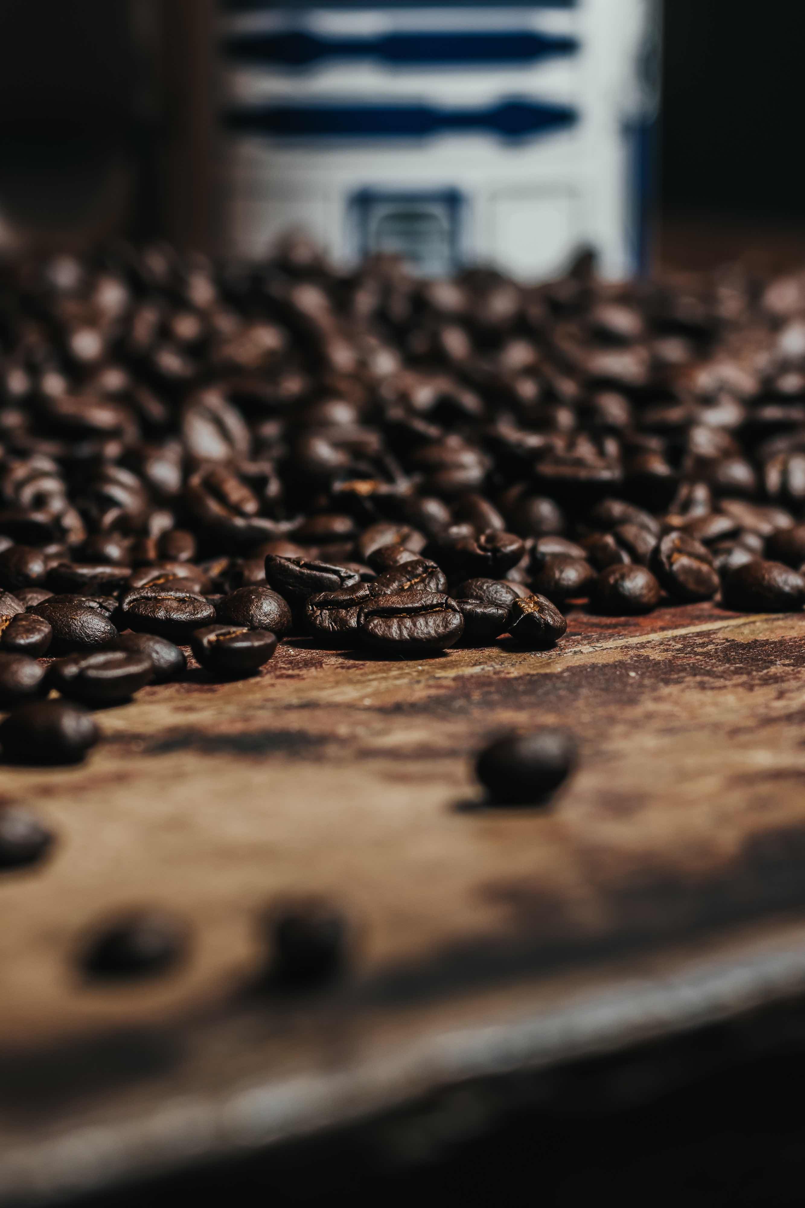 A pile of coffee beans near the edge of a dark wooden countertop.