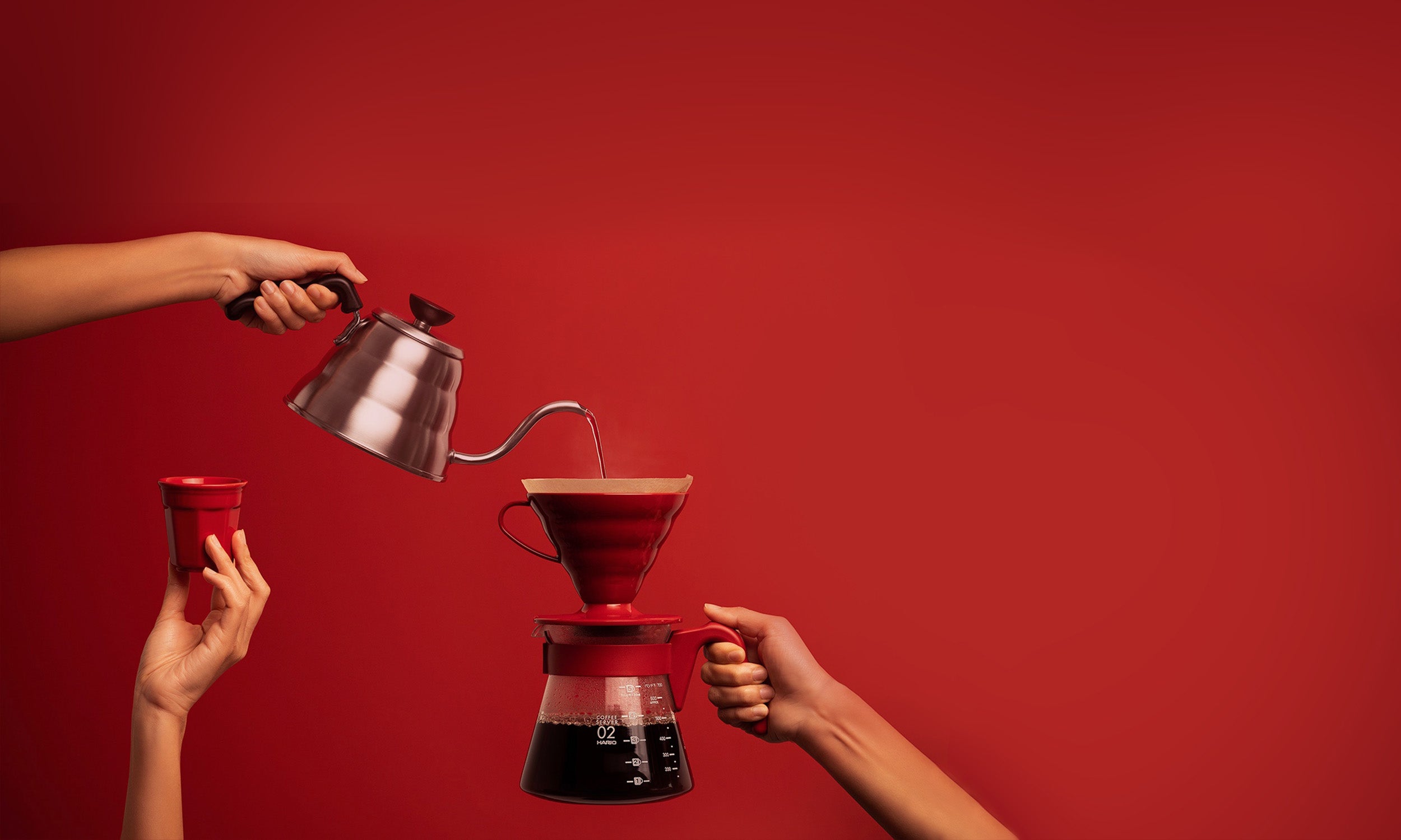 Image of hands brewing coffee in front of a red background.