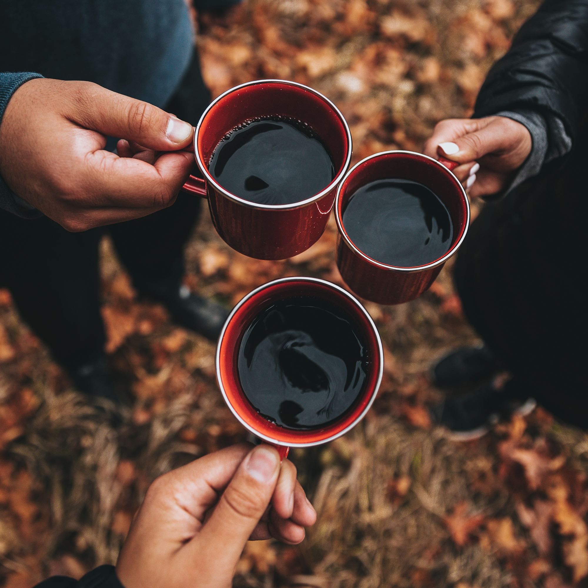 Three hands holding red coffee mugs outdoors.