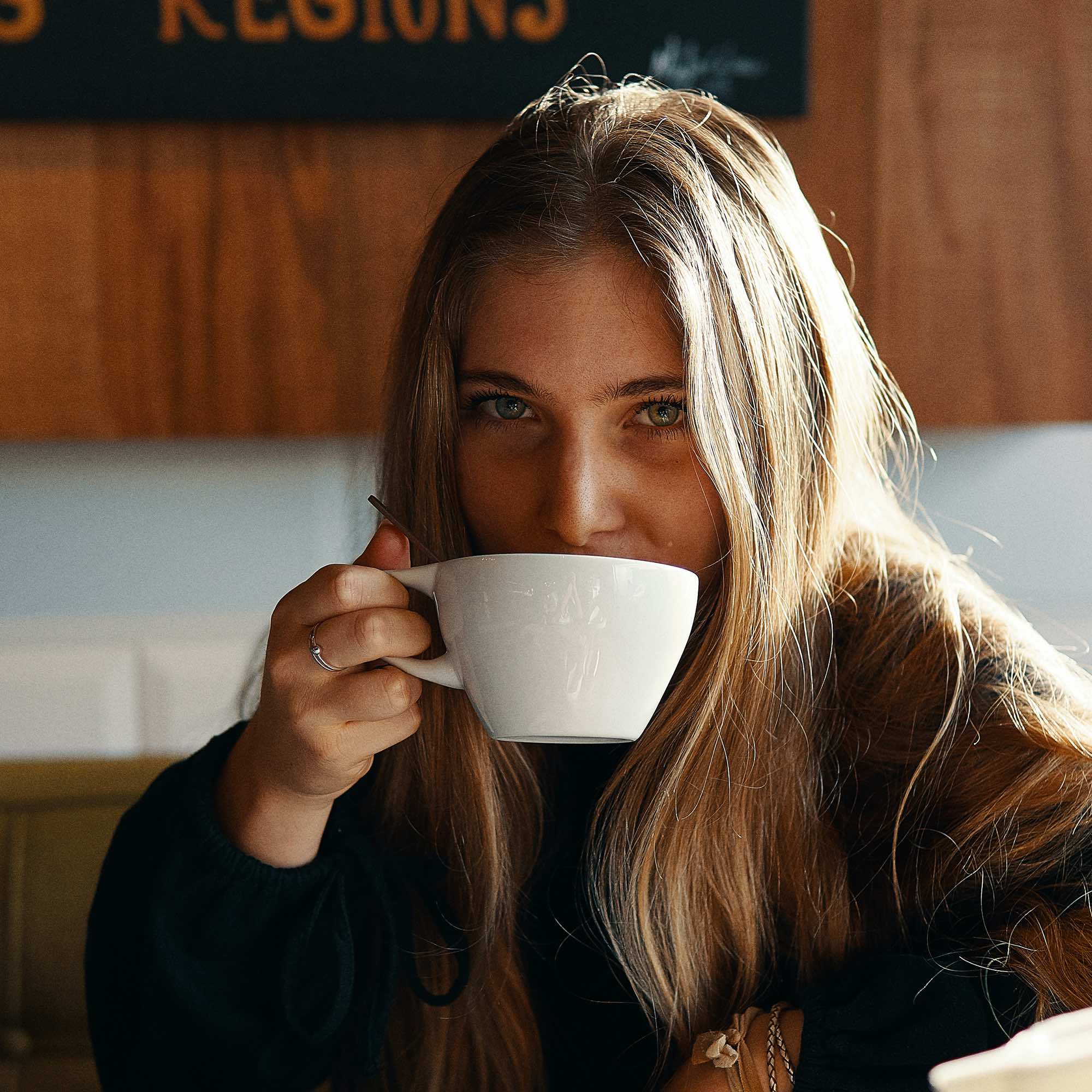 A woman sipping coffee from a white mug.